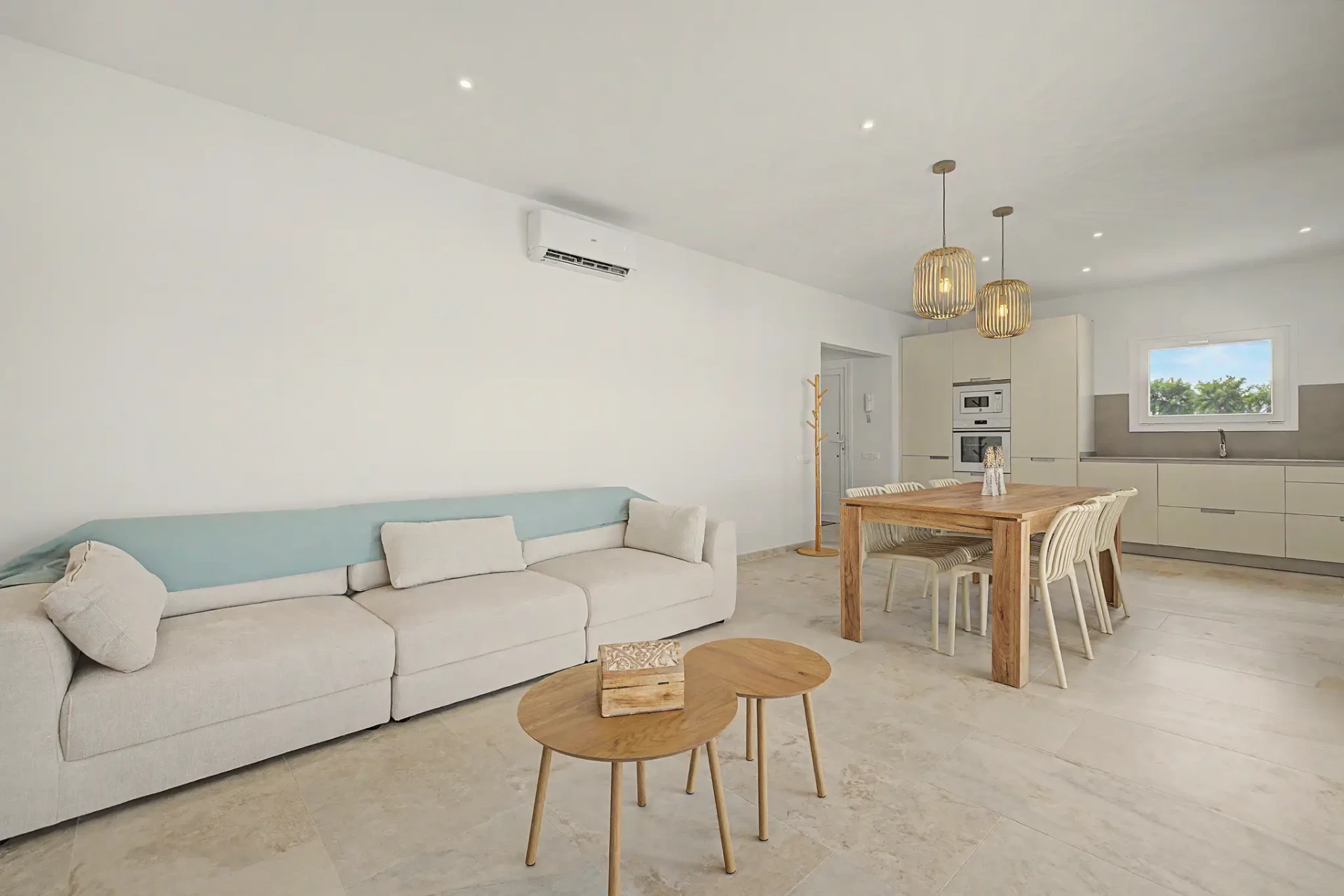 Salón con sofá largo, mesas bajas de madera y cocina abierta al fondo